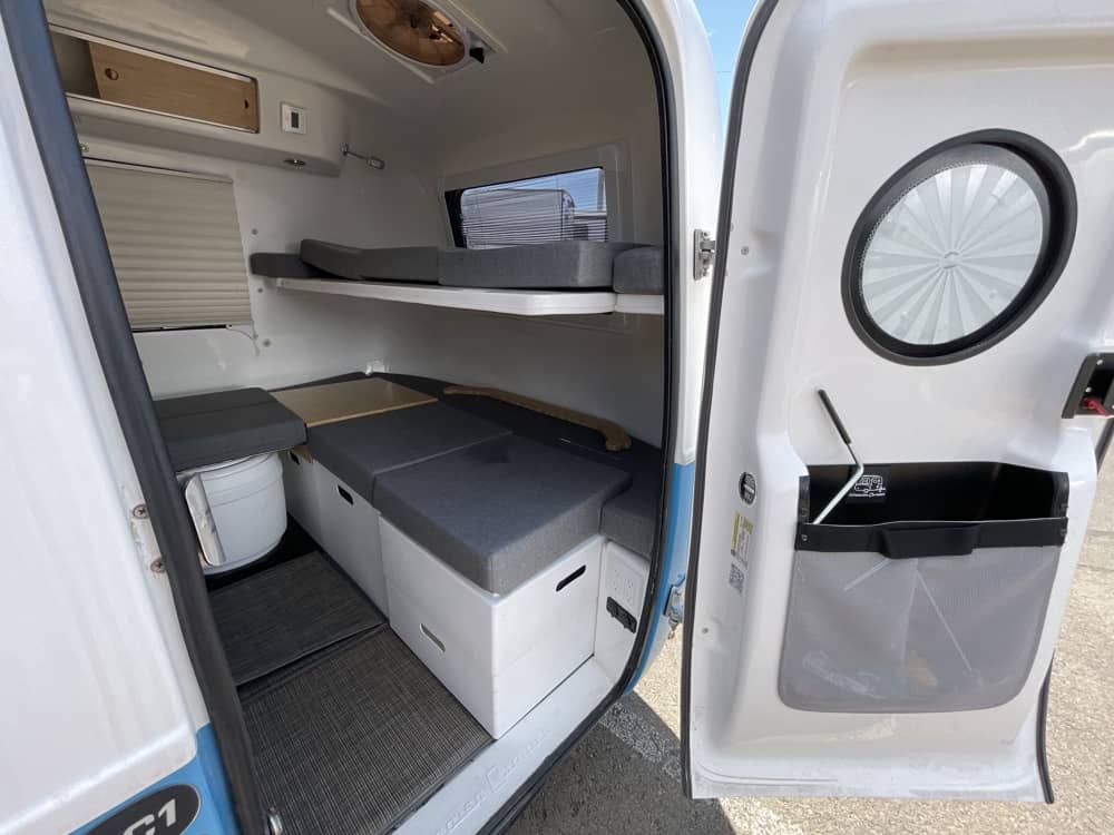 Interior view through open door showing Adaptiv modular cubes, shelf, and portable toilet